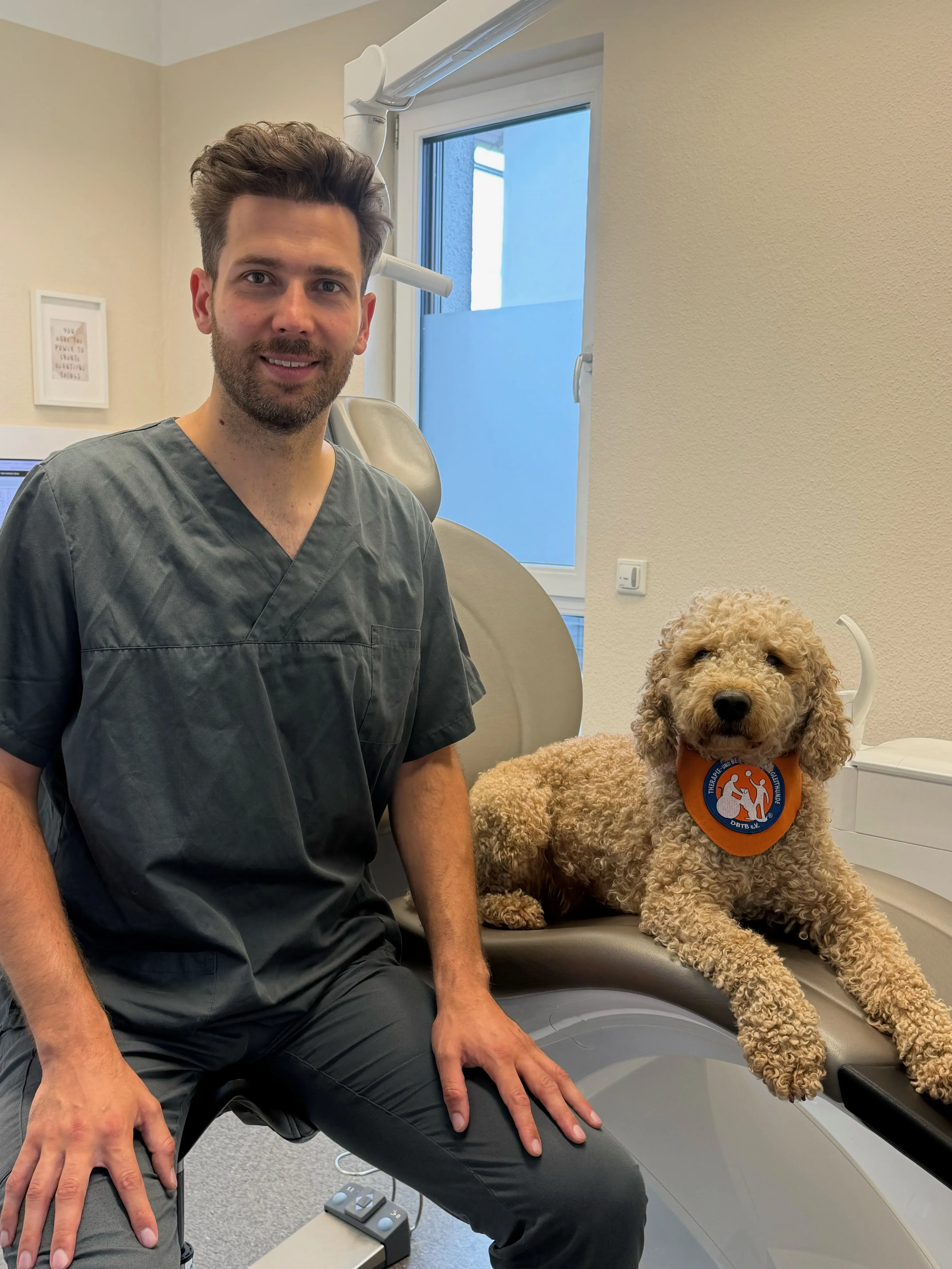 Zahnarzt der Praxis Zahnärzte im Rod sitzt entspannt neben Therapiehund Oskar im Behandlungszimmer