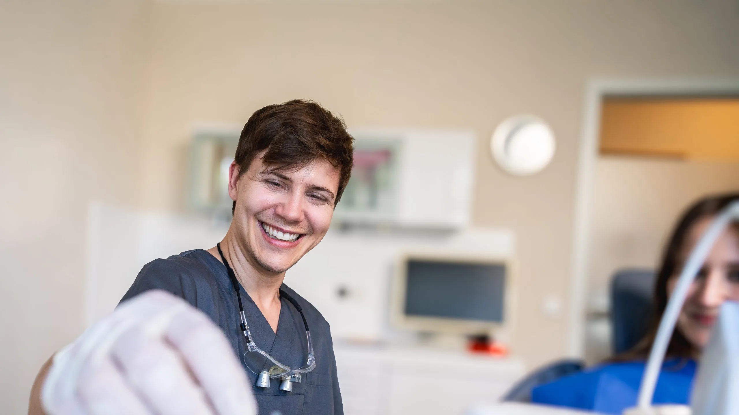 Lächelnder Zahnarzt begrüßt Patientin im Behandlungsraum und sorgt für eine angenehme Atmosphäre in der Zahnarztpraxis
